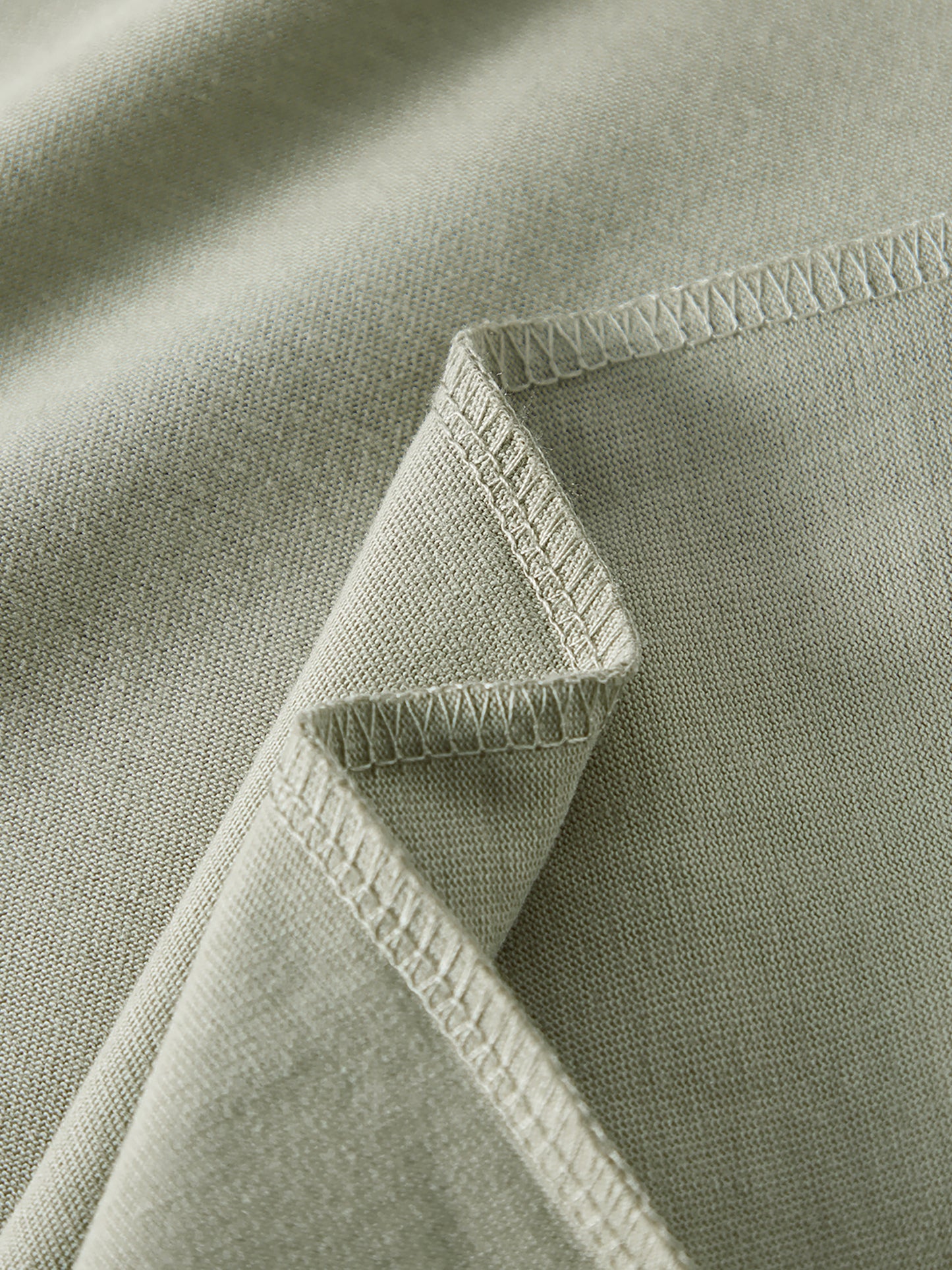 Close-up of a green fabric with a folded corner and visible stitching.