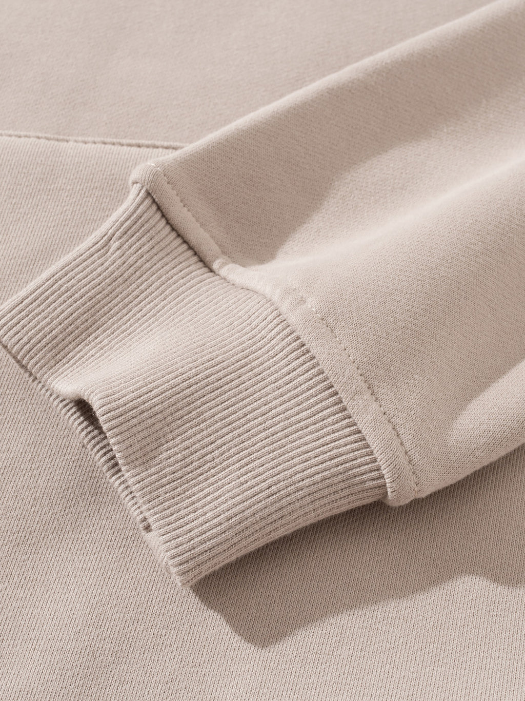 Close-up of a beige sweater sleeve with ribbed texture.