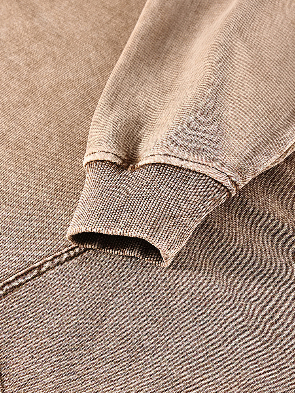 Close-up of a brown sweatshirt with ribbed cuffs and hem on a matching fabric background.