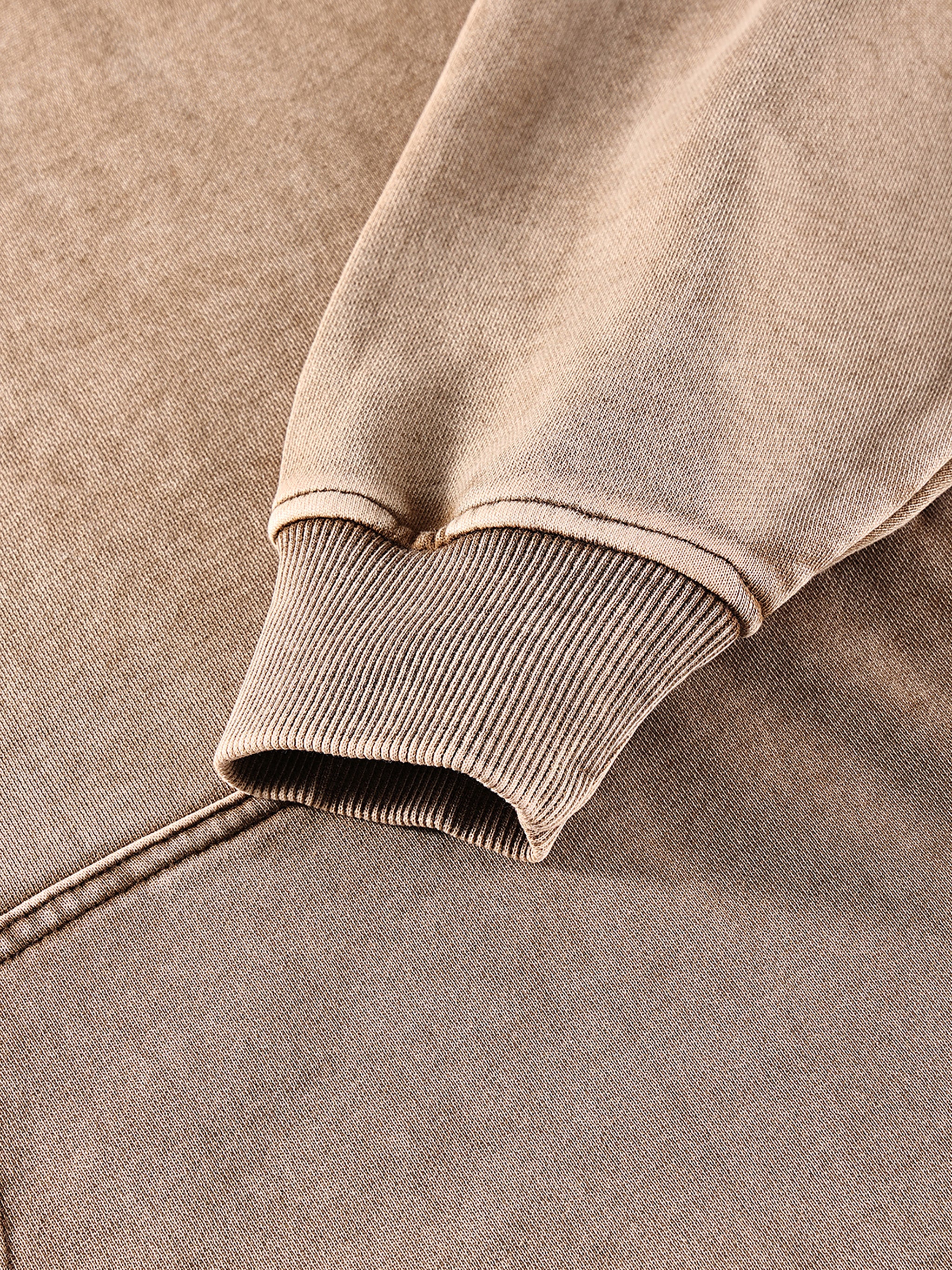 Close-up of a brown sweatshirt with ribbed cuffs and hem on a matching fabric background.