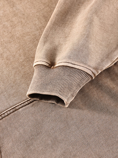 Close-up of a brown sweatshirt with ribbed cuffs and hem on a matching fabric background.