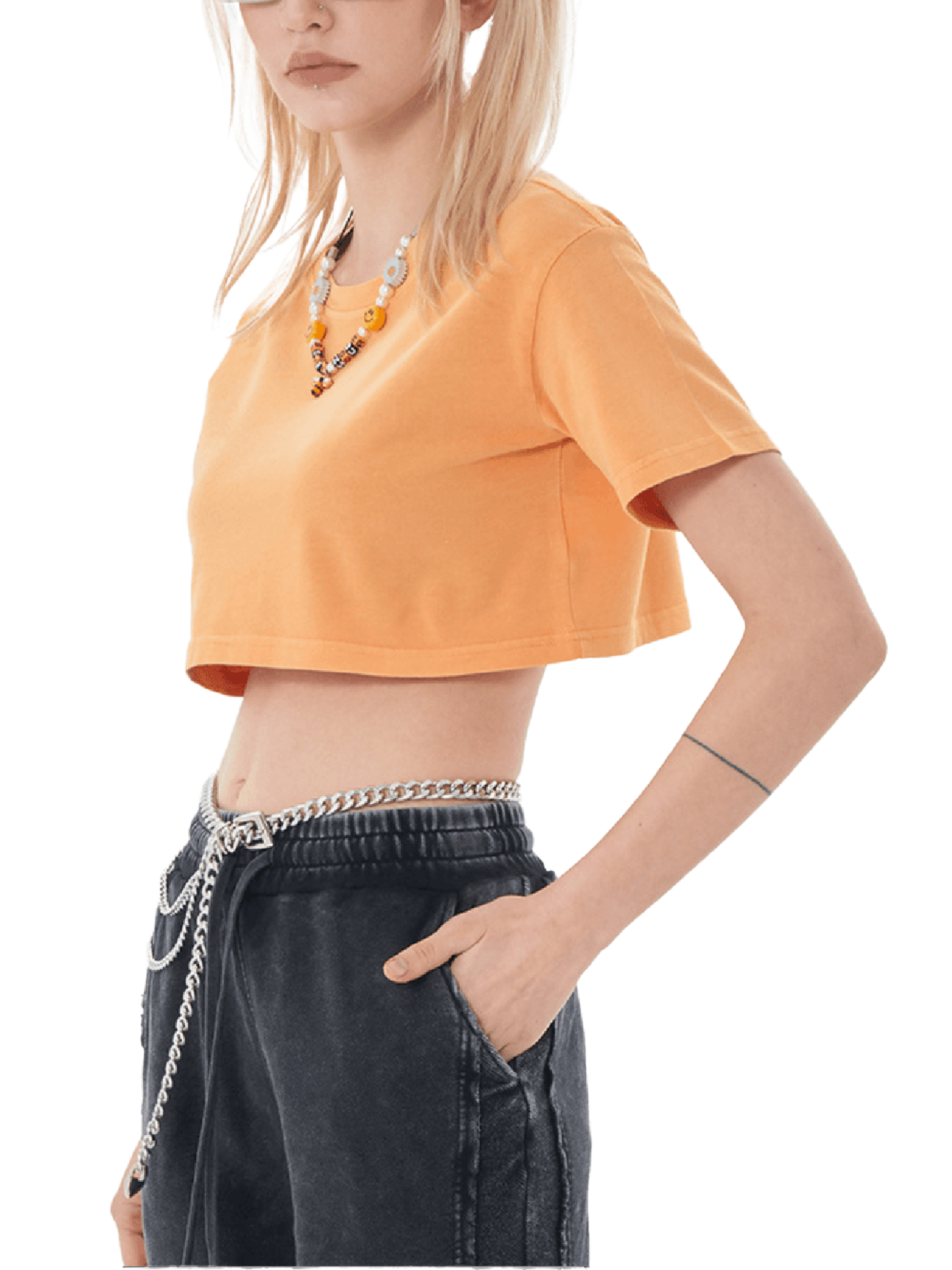 Person wearing an orange crop top and dark jeans with a chain detail on a white background