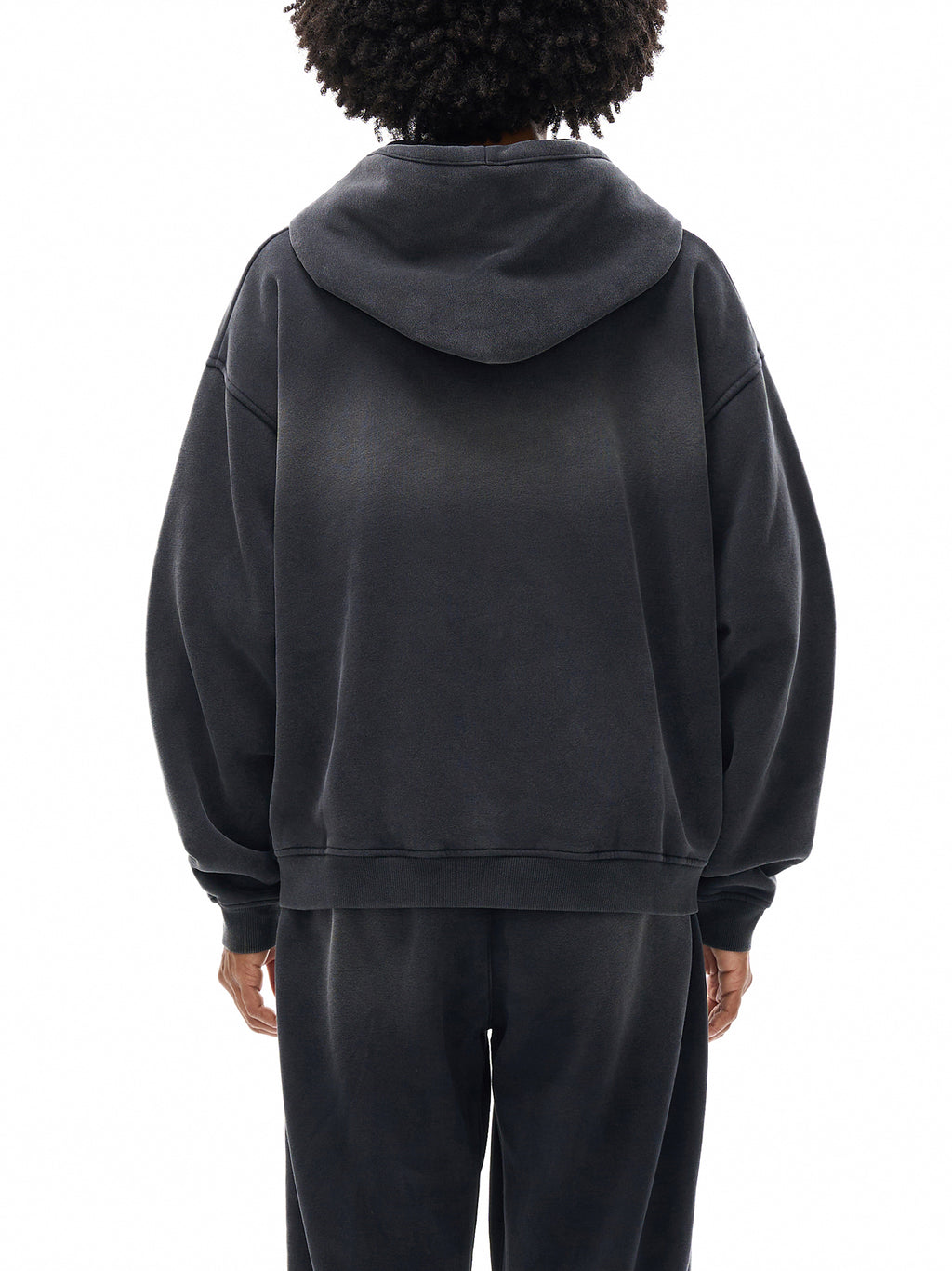 Person wearing a black hoodie and pants on a white background
