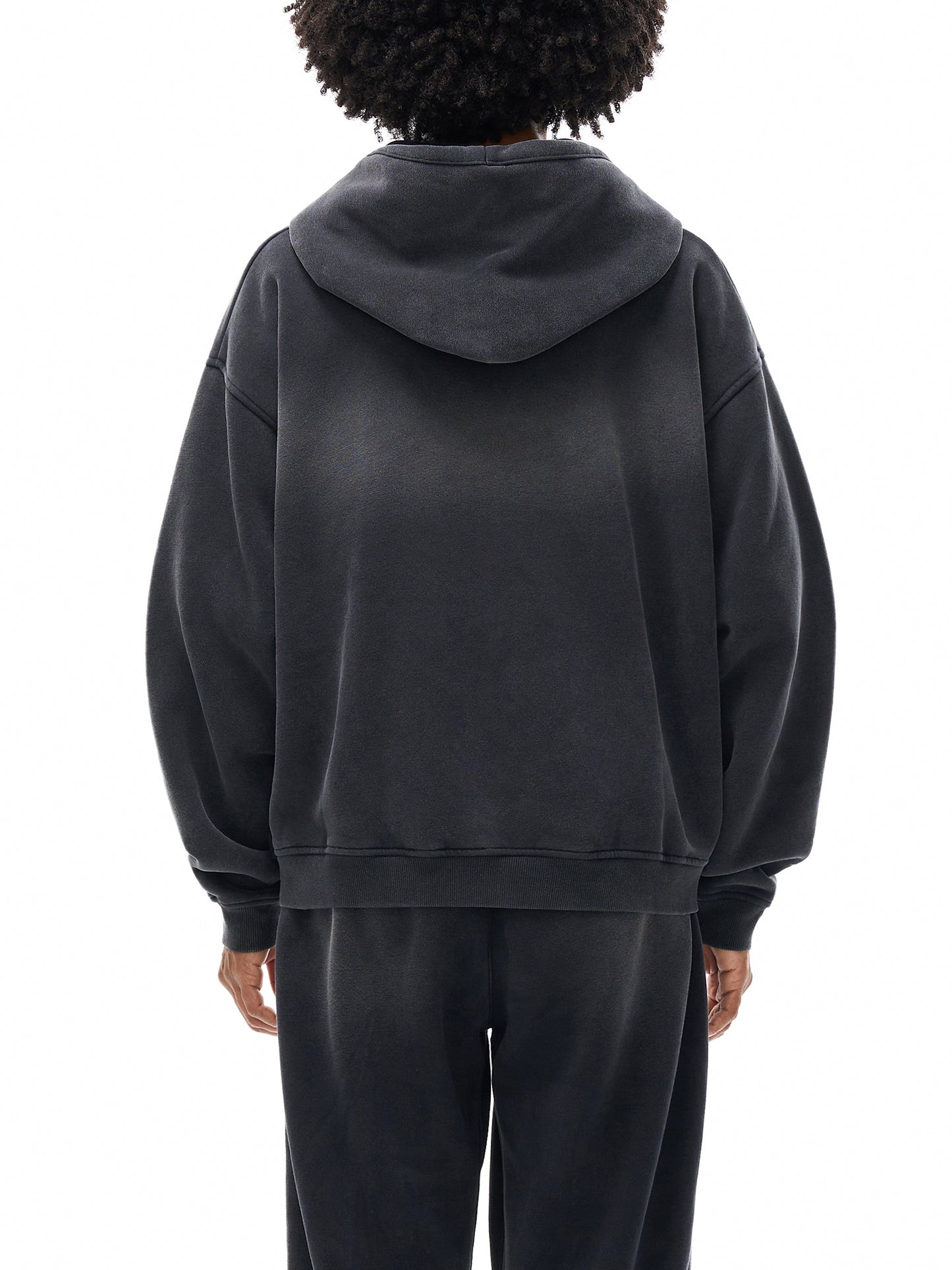 Person wearing a black hoodie and pants on a white background