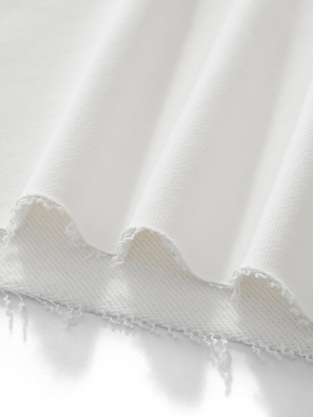 Close-up of white fabric with a ruffled edge on a light gray background