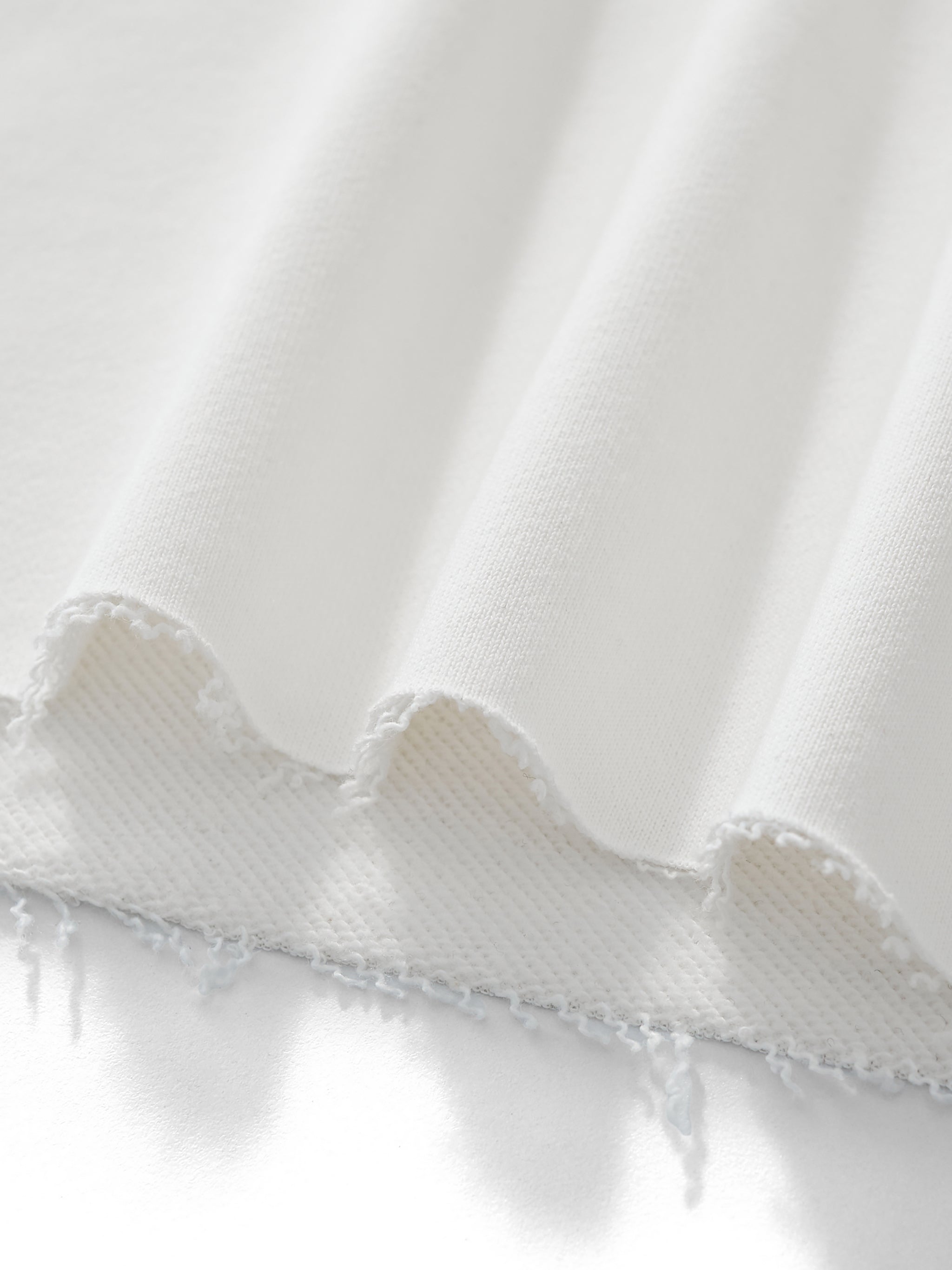Close-up of white fabric with a ruffled edge on a light gray background